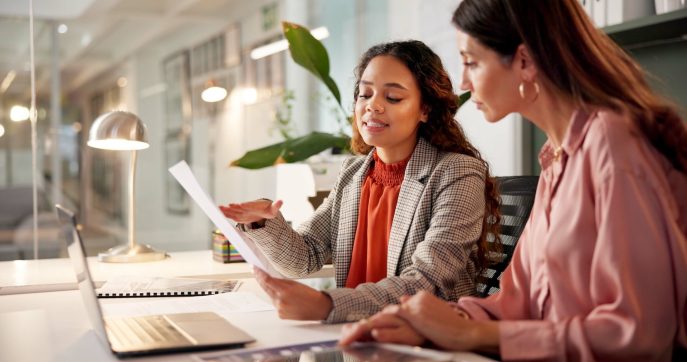 Two businesswomen reviewing financial documents and ROI metrics at a desk