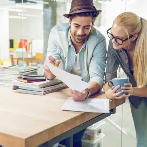 Two young professionals discussing documents in a modern office setting