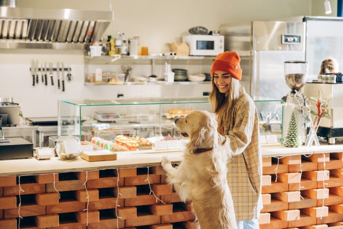 Smiling woman in beanie and flannel shirt with golden retriever at a bakery counter