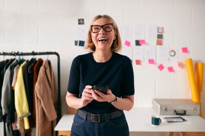 Confident businesswoman smiling while holding a phone in a creative workspace