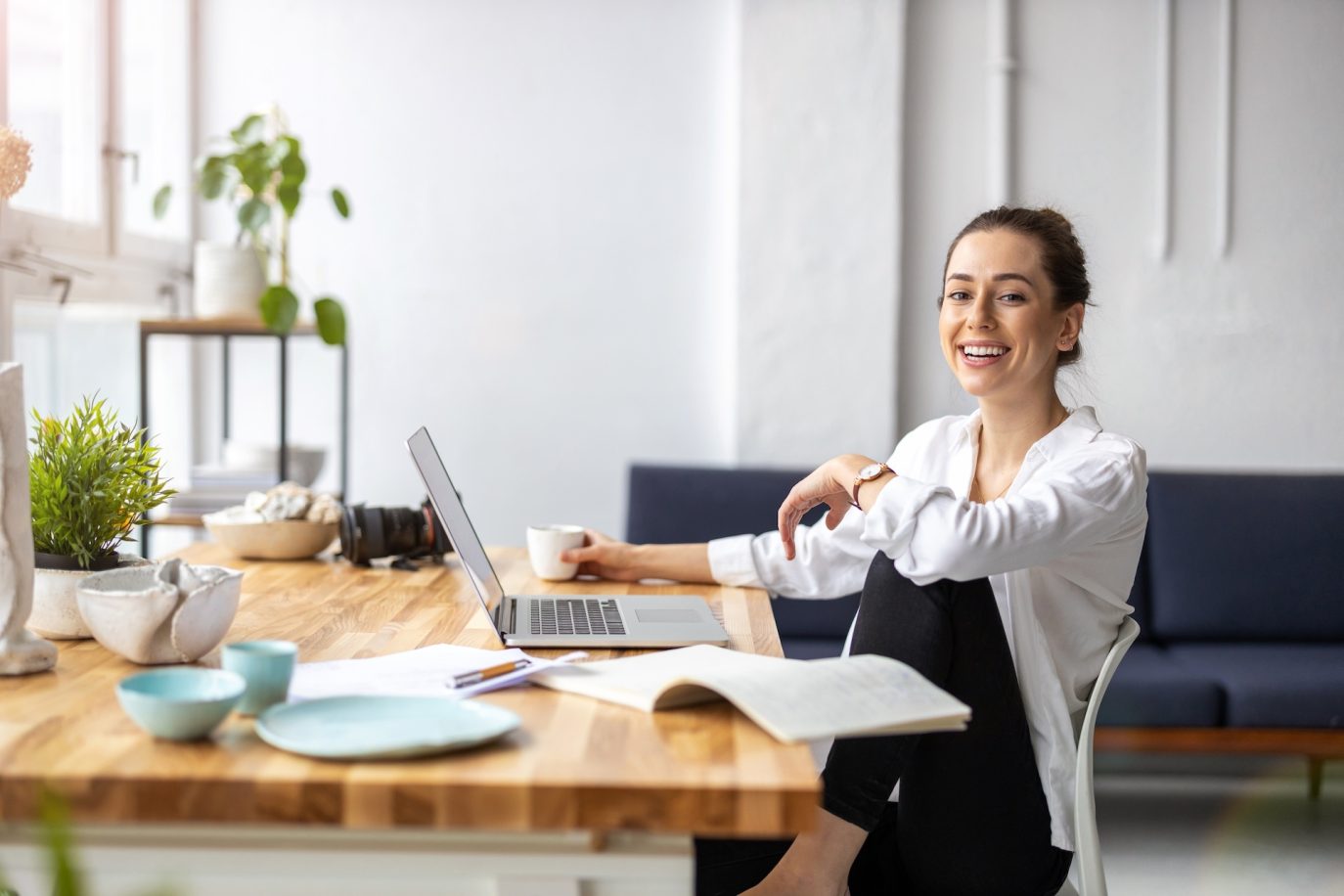 Smiling young entrepreneur working from home with laptop and coffee