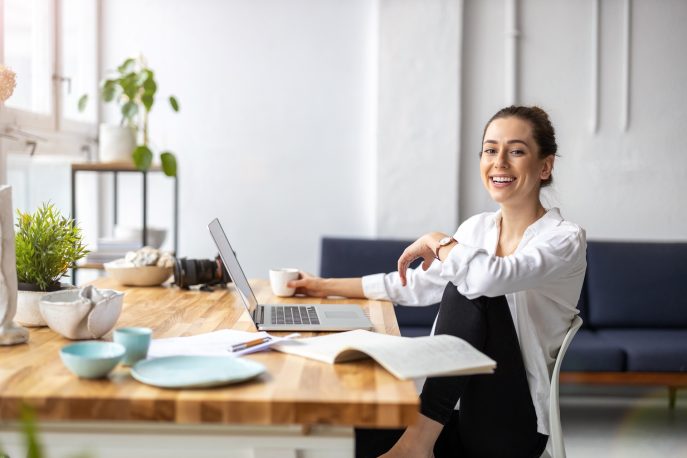 Smiling young entrepreneur working from home with laptop and coffee