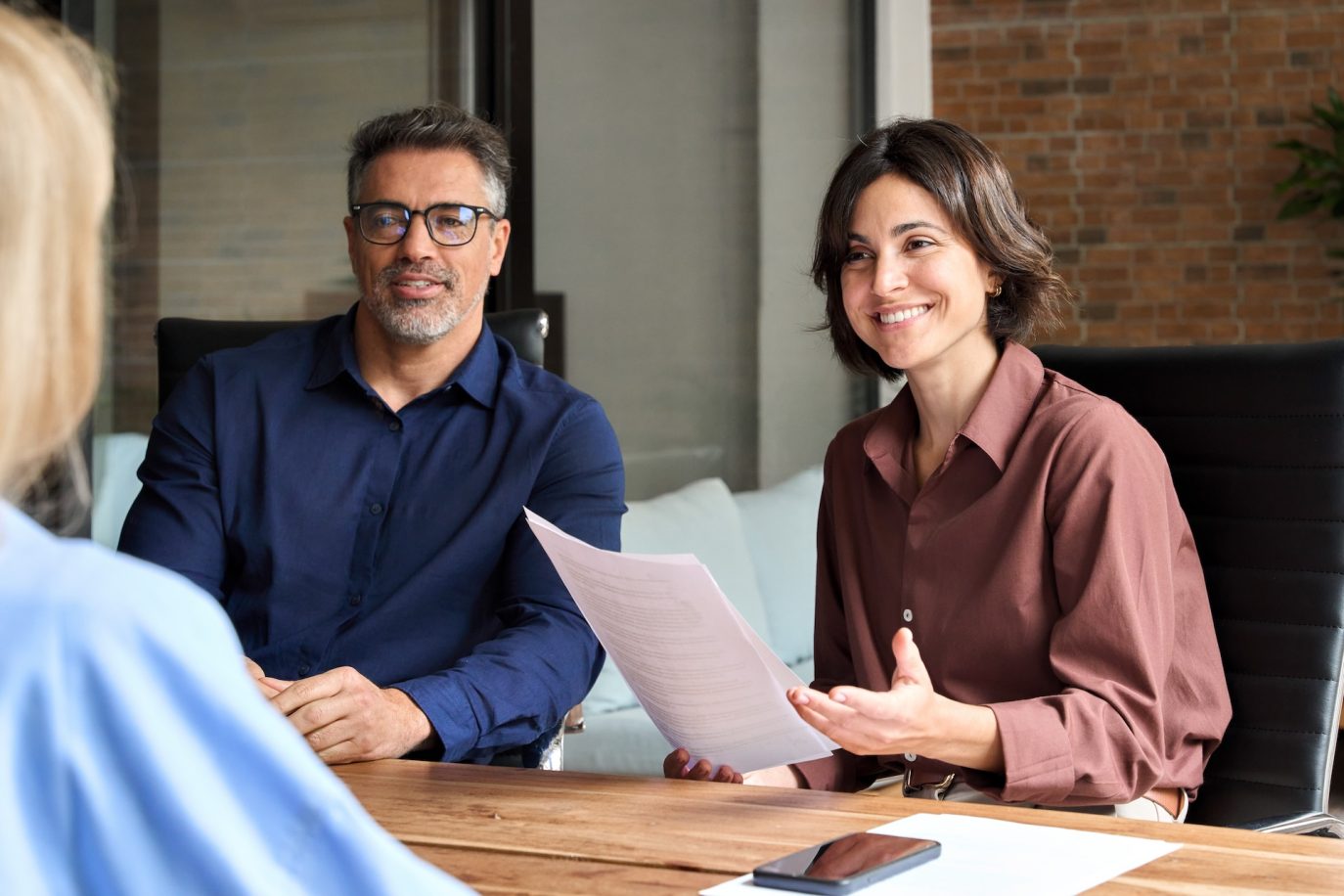 Two business professionals in a meeting with a client, smiling and holding documents