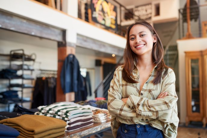 Confident young clothing store owner standing inside her boutique