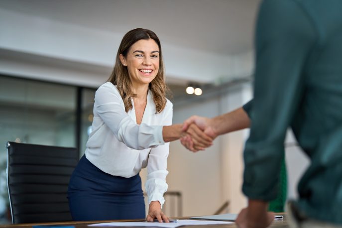 Smiling businesswoman shaking hands across a desk in a modern office