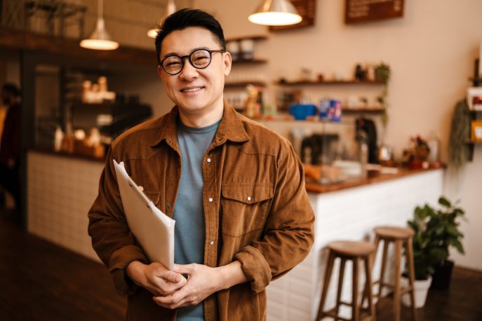 Confident small business owner holding paperwork inside his cozy cafe