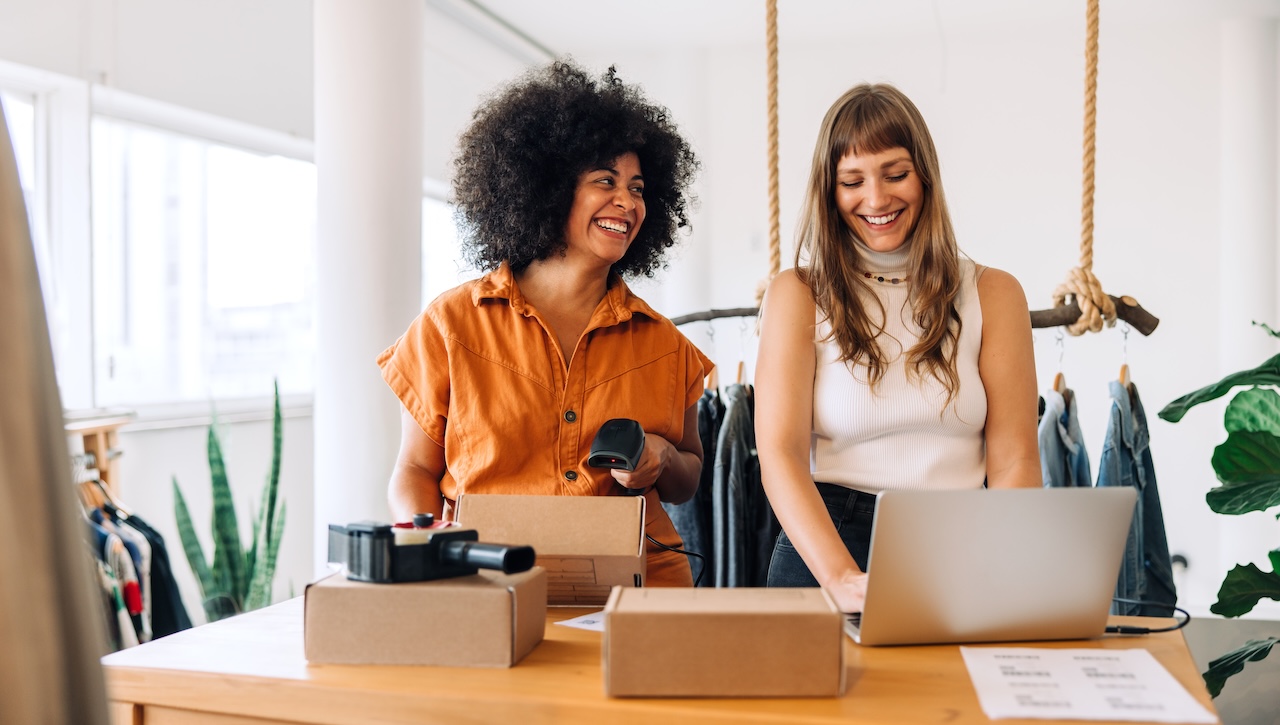 Two smiling small business owners preparing online orders in a modern clothing boutique
