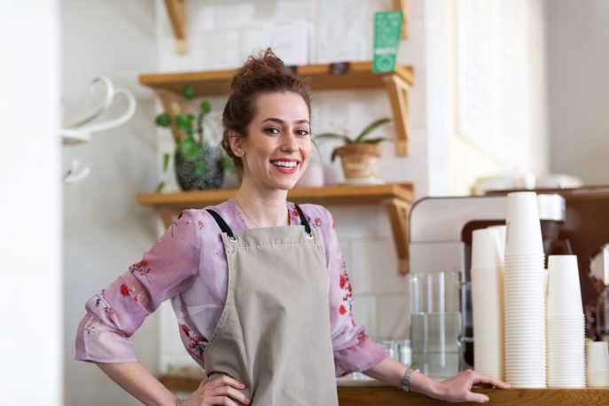 Young café owner smiling behind the counter next to takeaway coffee cups