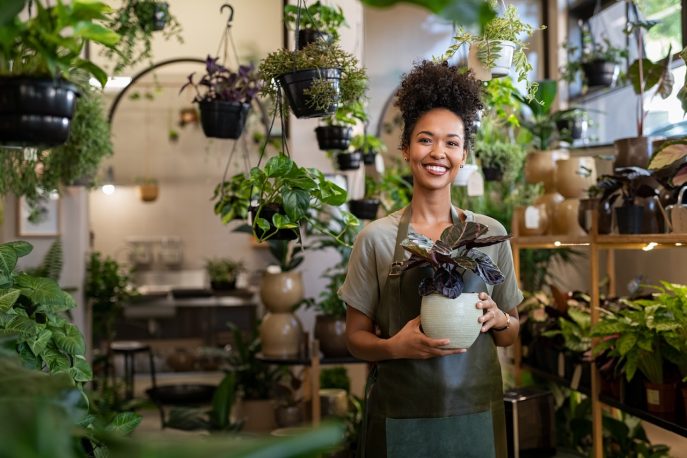 Female plant shop owner holding potted plant and smiling inside her business