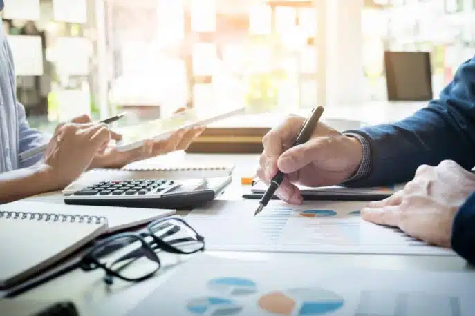Two professionals reviewing financial charts with a calculator and tablet at a desk