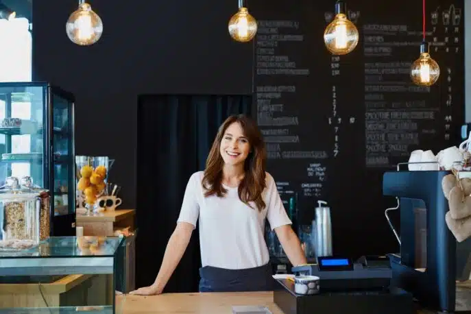 Smiling café owner standing behind the counter in a modern coffee shop