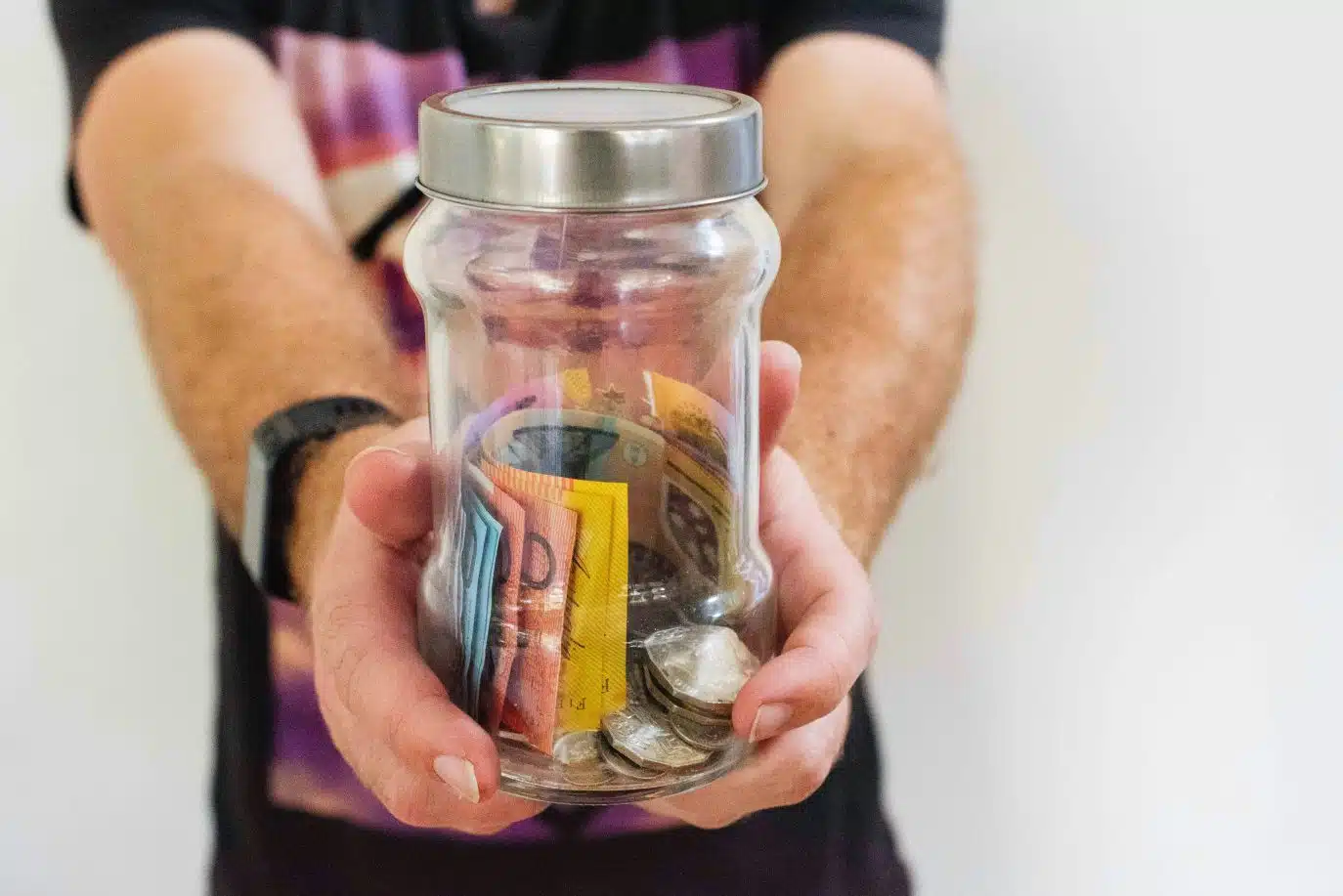 Person holding a glass jar filled with Australian coins and banknotes.