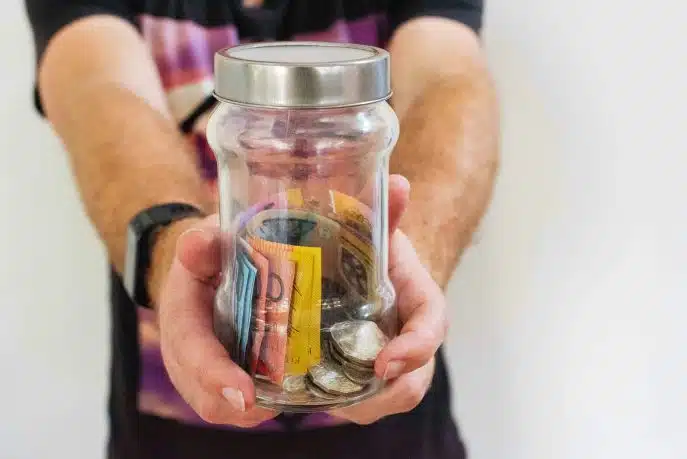 Person holding a glass jar filled with Australian coins and banknotes.