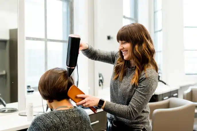 Smiling hairdresser blow drying a customer’s hair in a modern salon