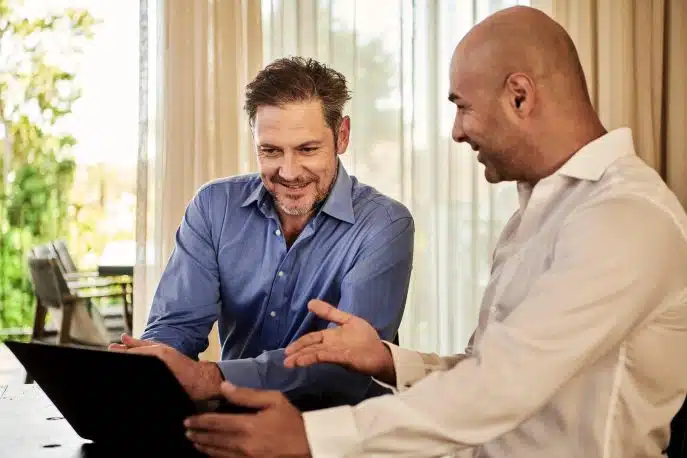 Two businessmen discussing something on a laptop at a desk in a well-lit office