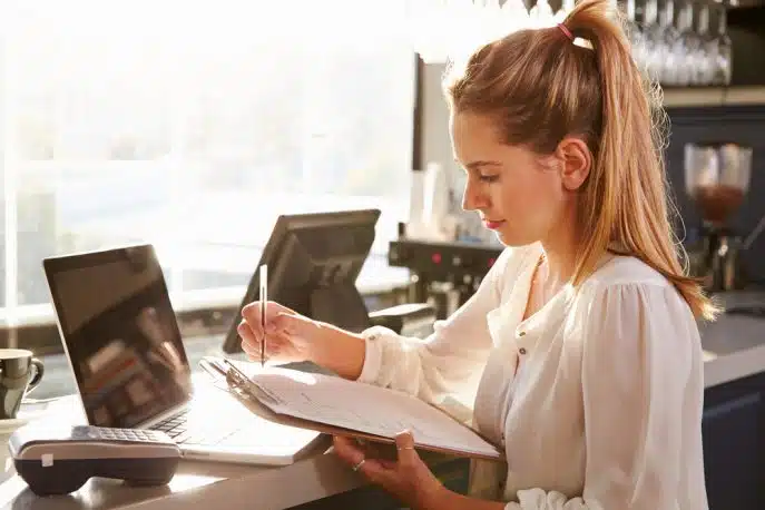 Young woman reviewing paperwork at a café counter with a laptop