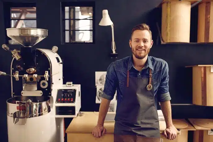 Coffee roaster business owner smiling beside industrial roasting equipment