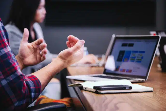 Close-up of hands gesturing during a business discussion with laptop and smartphone on the table