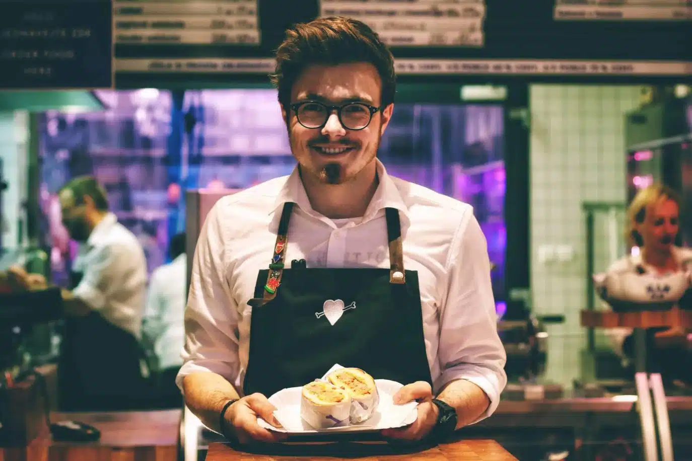 Smiling male café employee holding a sandwich in a vibrant food service environment