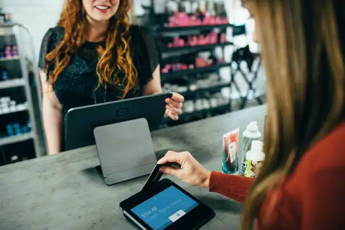 Customer inserting credit card into a tablet payment terminal at a retail counter, with a smiling cashier in the background.