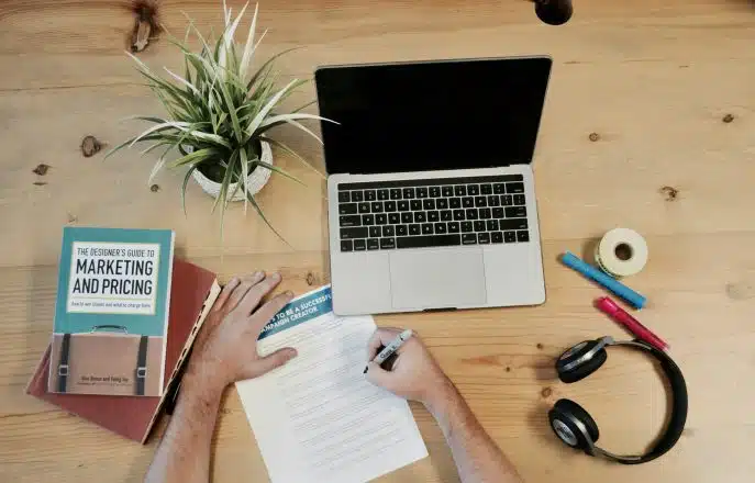 Overhead view of a person working at a wooden desk with a laptop, marketing book, and campaign notes.