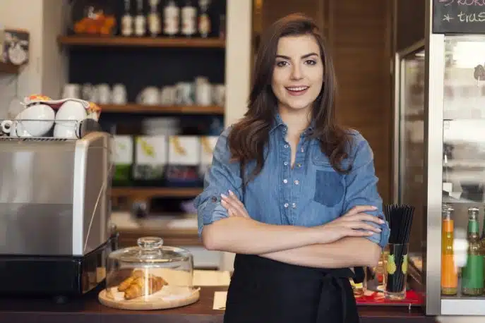 Confident female café owner standing behind the counter