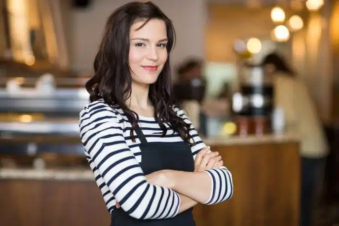 Confident female café owner with crossed arms in striped shirt and apron