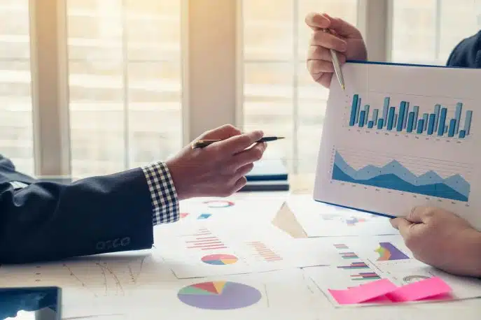 Close-up of two professionals analyzing financial charts and graphs at a desk with reports and a tablet.