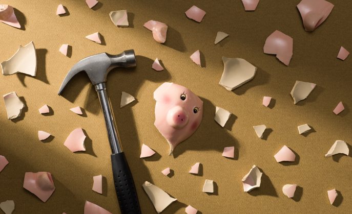 Broken piggy bank shattered with hammer surrounded by ceramic pieces