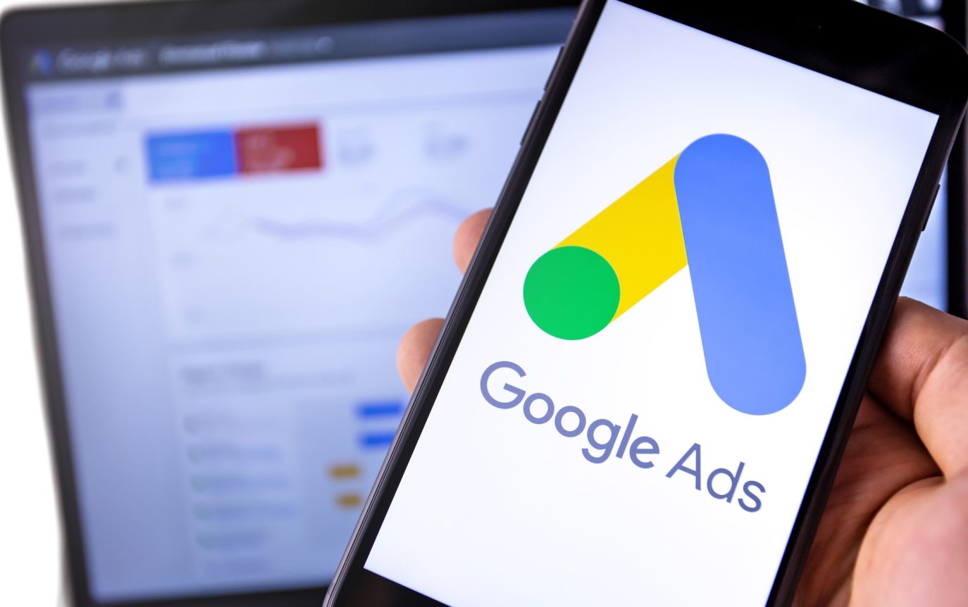 Mobile phone displaying Google Ads logo in front of campaign analytics screen