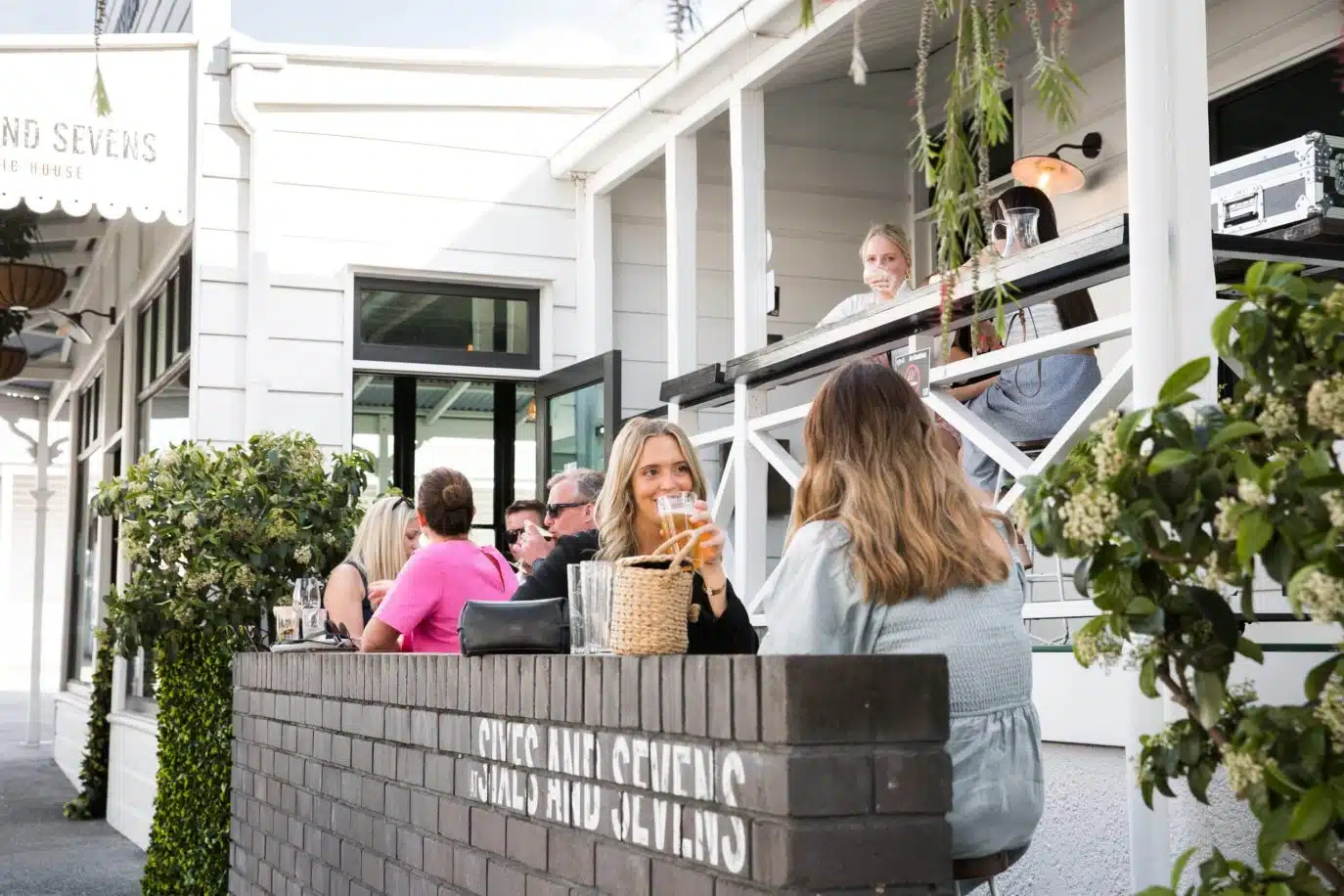 Group of people enjoying drinks on a sunlit patio outside a modern cafe