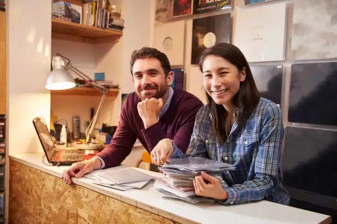 Smiling business partners at a record store counter surrounded by vinyls and CDs