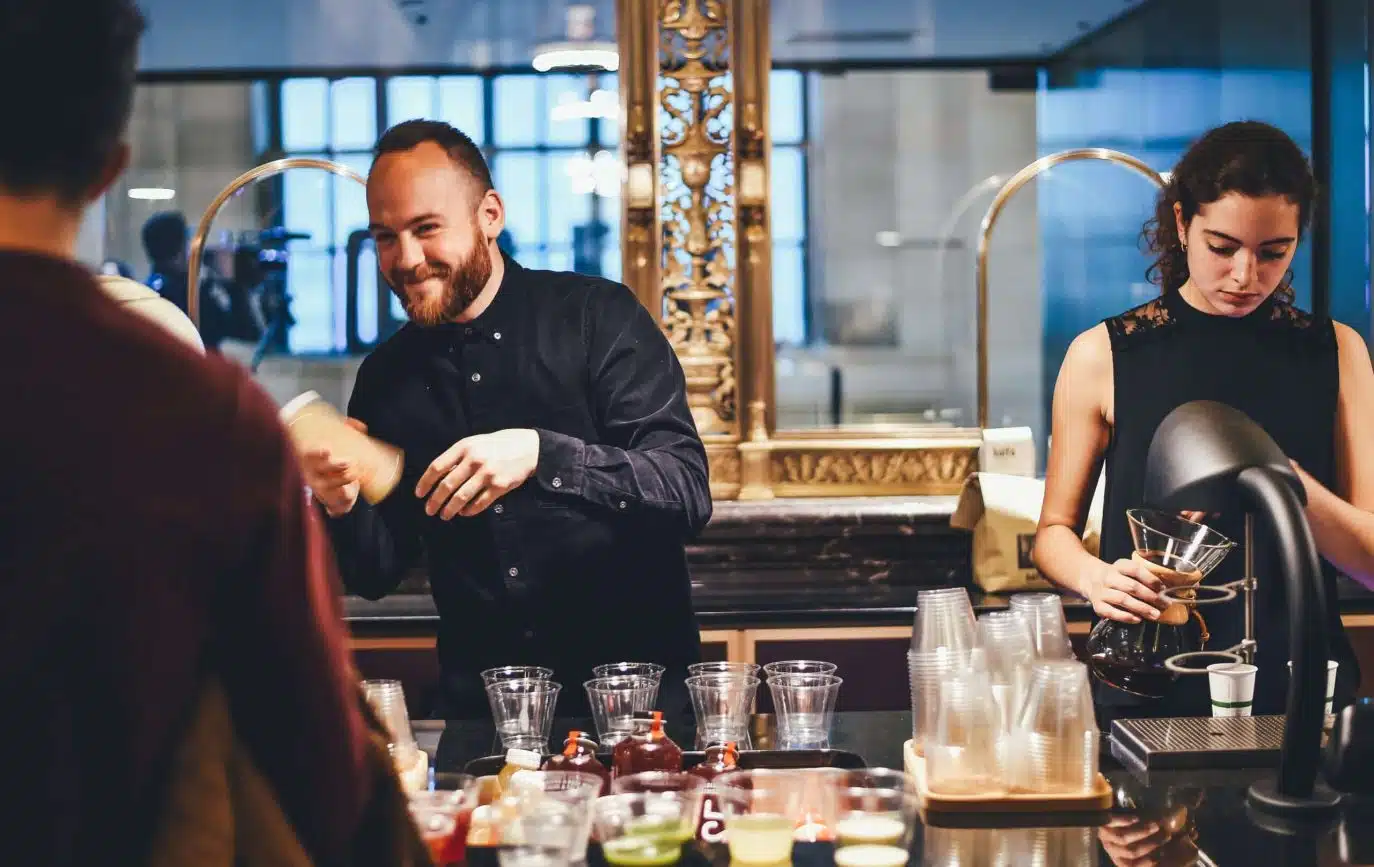 Barista duo preparing drinks behind a café counter with a smiling male barista and focused female barista