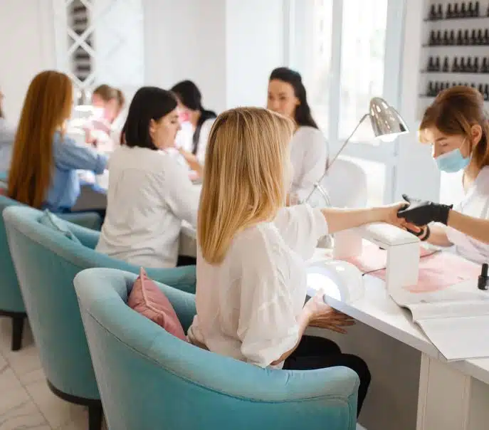 Customers receiving manicures at a busy modern nail salon with technicians wearing protective gloves and masks.
