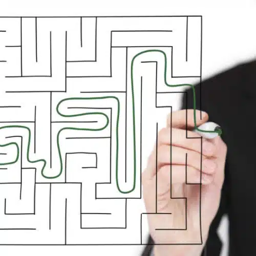Hand drawing a path through a business maze on transparent board