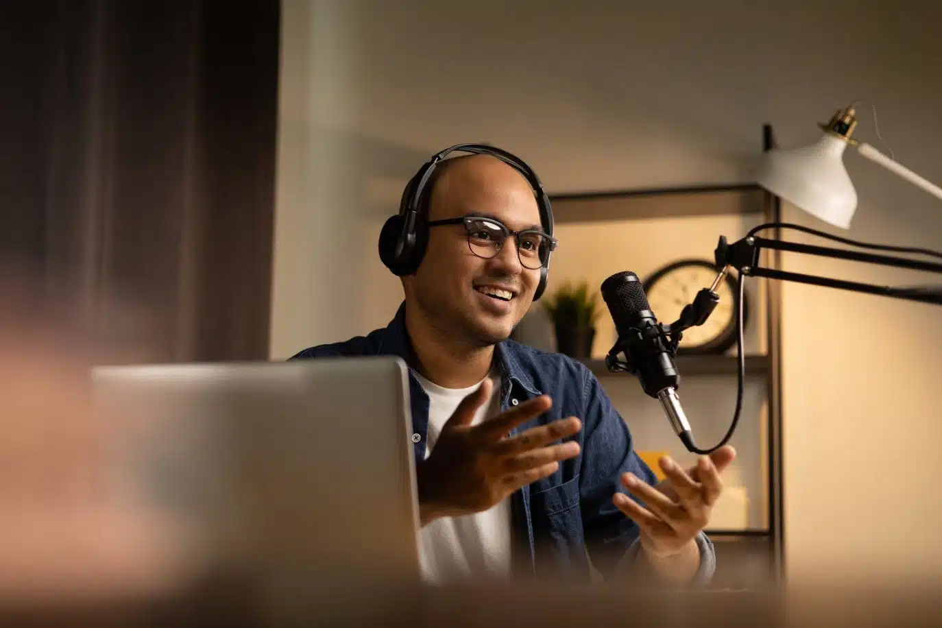 Man wearing headphones speaking into a microphone during a podcast recording at home.