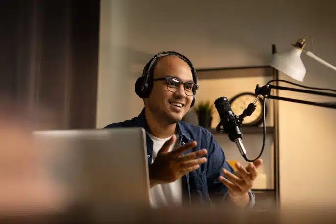 Man wearing headphones speaking into a microphone during a podcast recording at home.