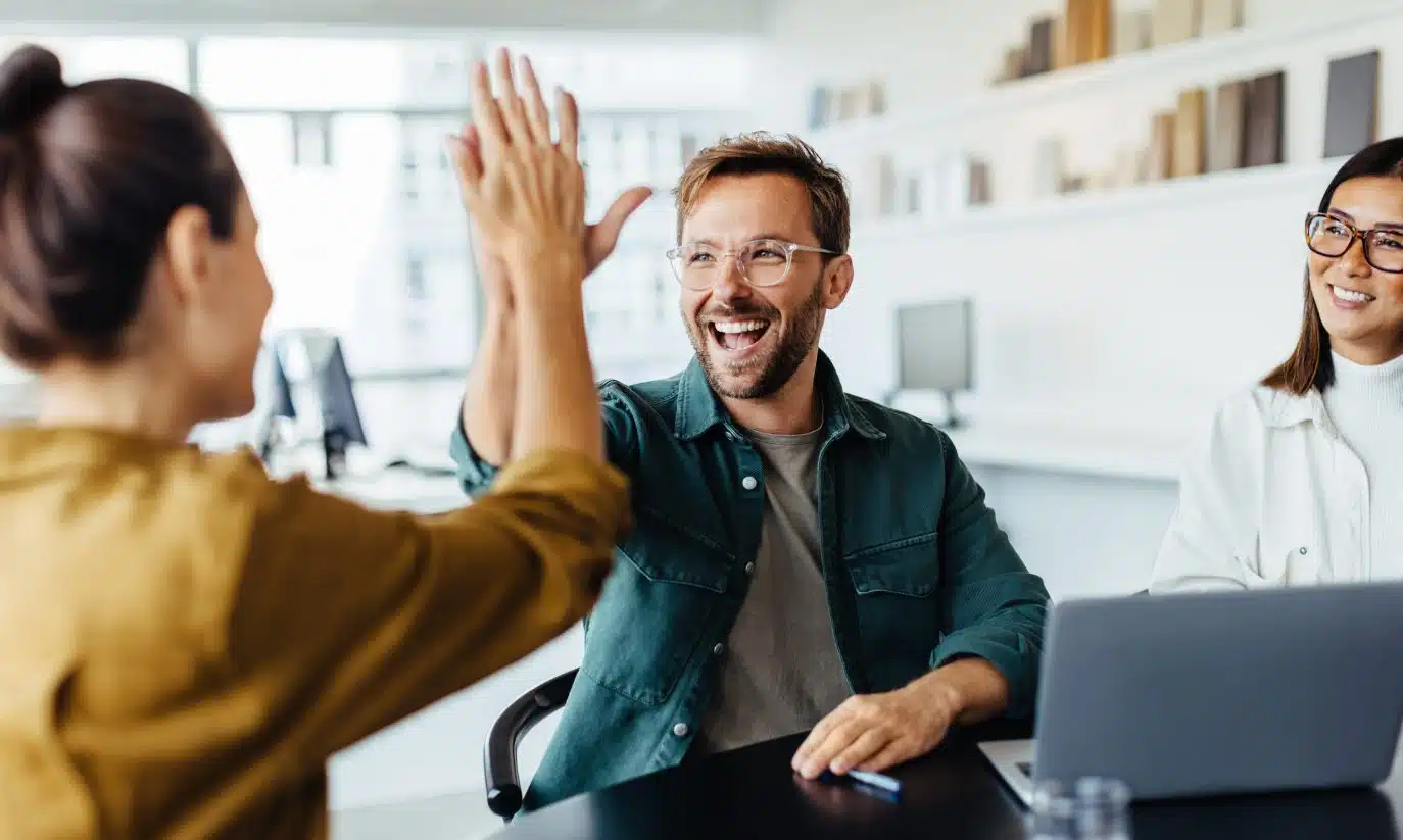 Team members celebrating success with a high-five in a modern office setting.