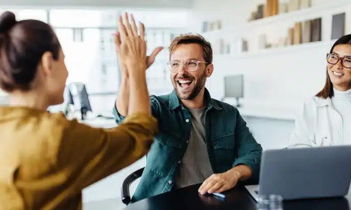Team members celebrating success with a high-five in a modern office setting.