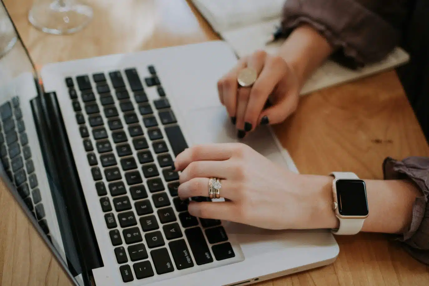 Close-up of a woman's hands typing on a laptop, wearing rings and a smartwatch.