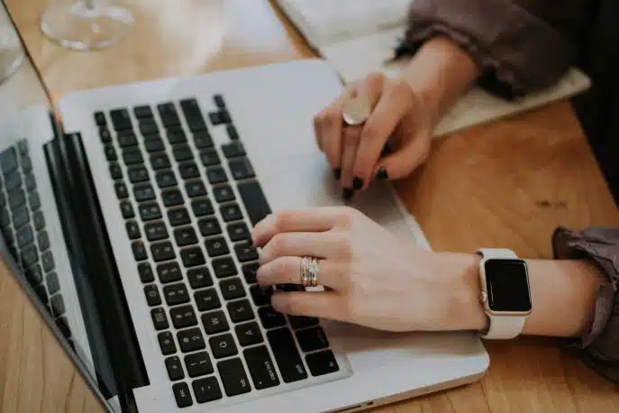 Close-up of a woman's hands typing on a laptop, wearing rings and a smartwatch.