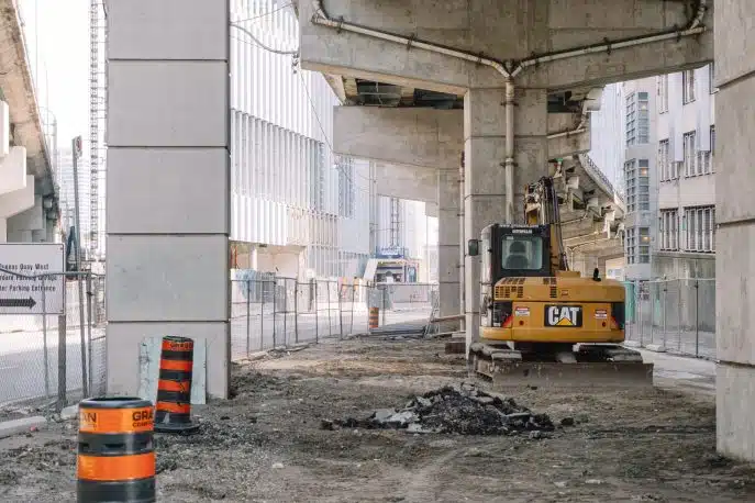 Construction site under highway overpass with excavator and traffic barrels