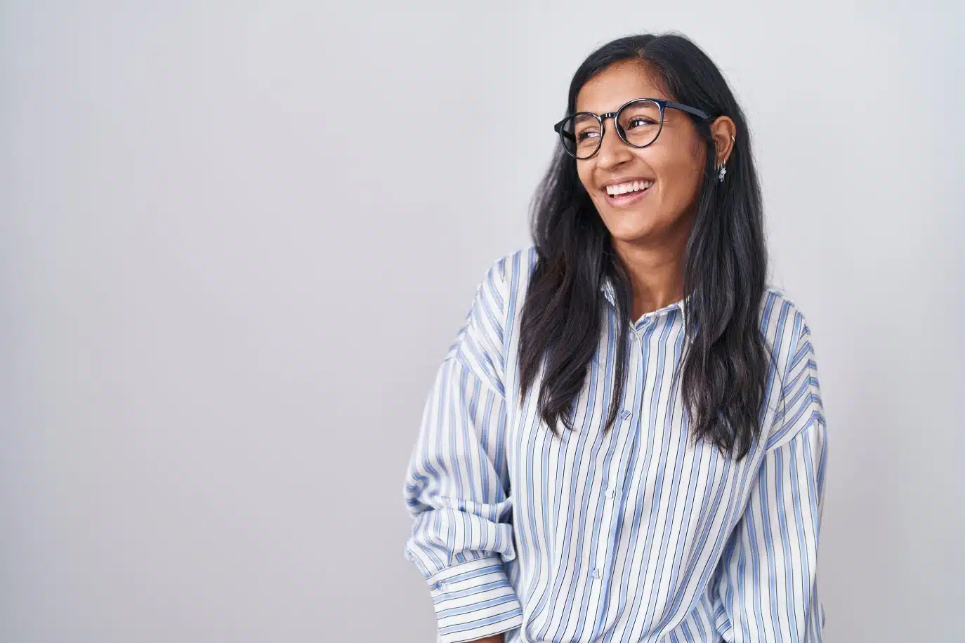 Confident young woman in glasses smiling in front of a plain light background.