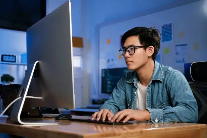 Focused young developer working at his desk on a large computer monitor in a modern office environment.