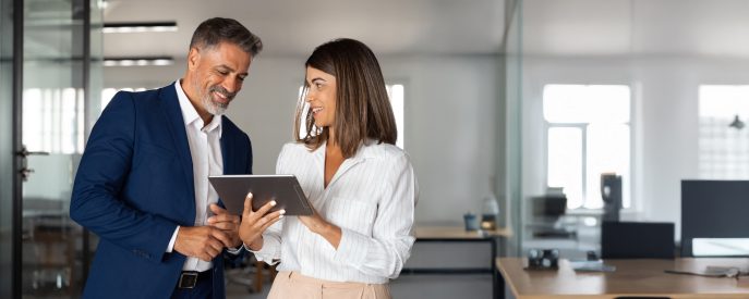 Two professionals discussing business growth strategies while reviewing information on a digital tablet in a modern office setting.