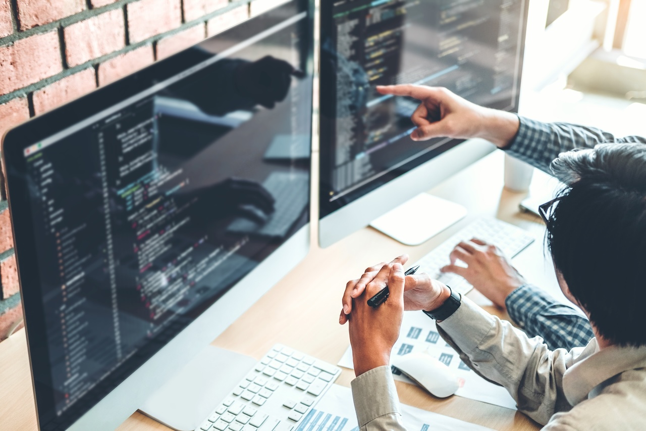 Two developers discussing code on computer monitors