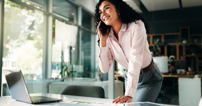Smiling businesswoman on phone call at office desk with open laptop