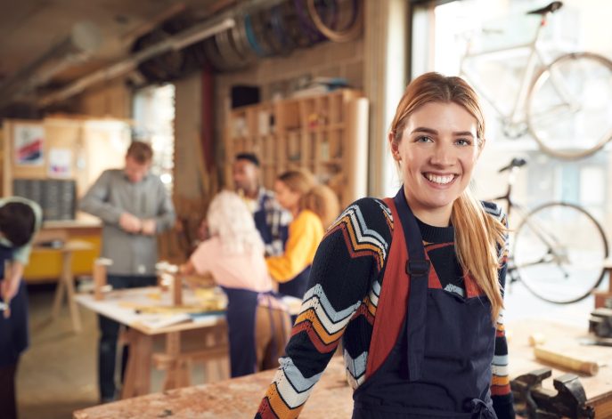 Smiling young woman in an apron standing confidently in a busy workshop