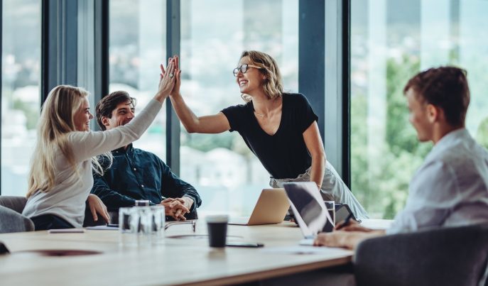 Team celebrating a business success with high-five in a modern office setting